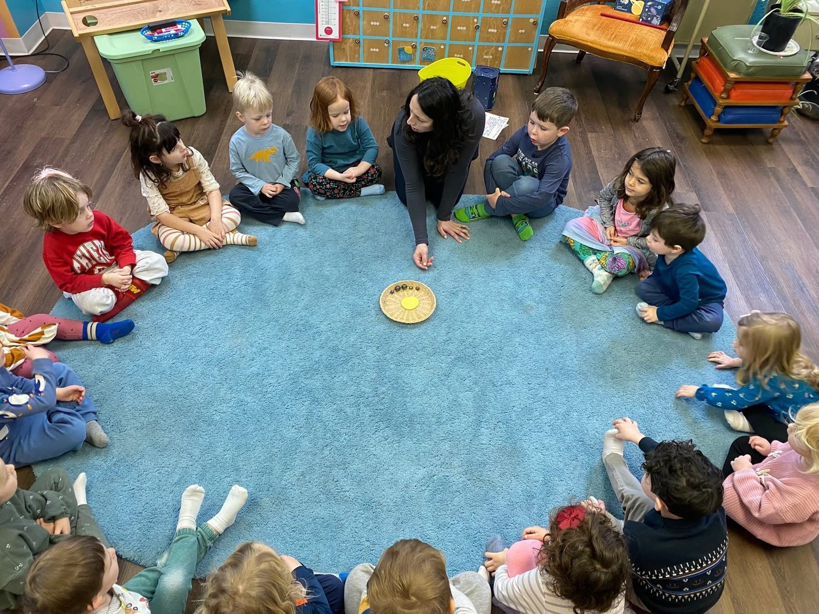 Teacher leading circle time with children seated around a blue rug